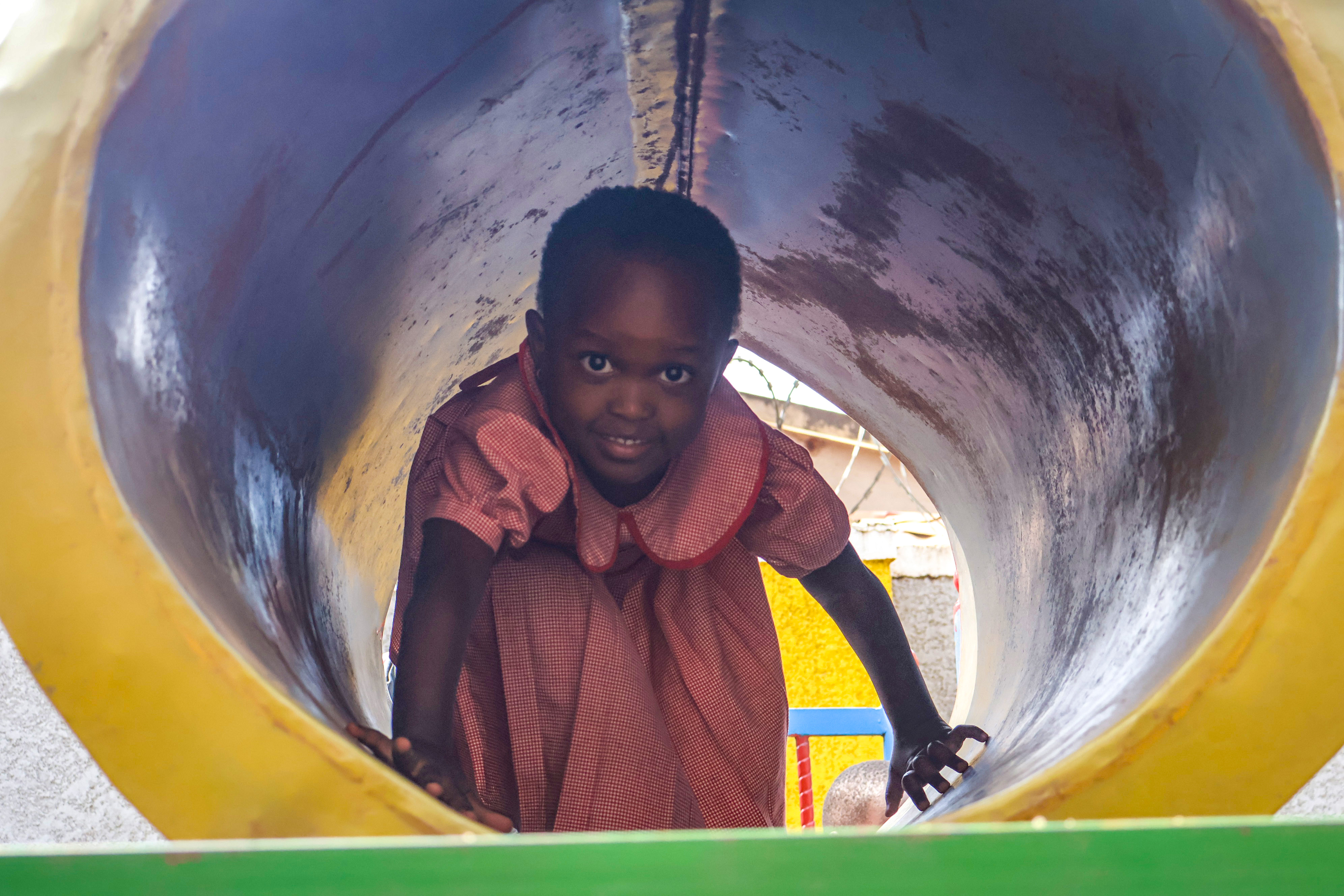 Student peeking out of the playground tunnel slide, smiling